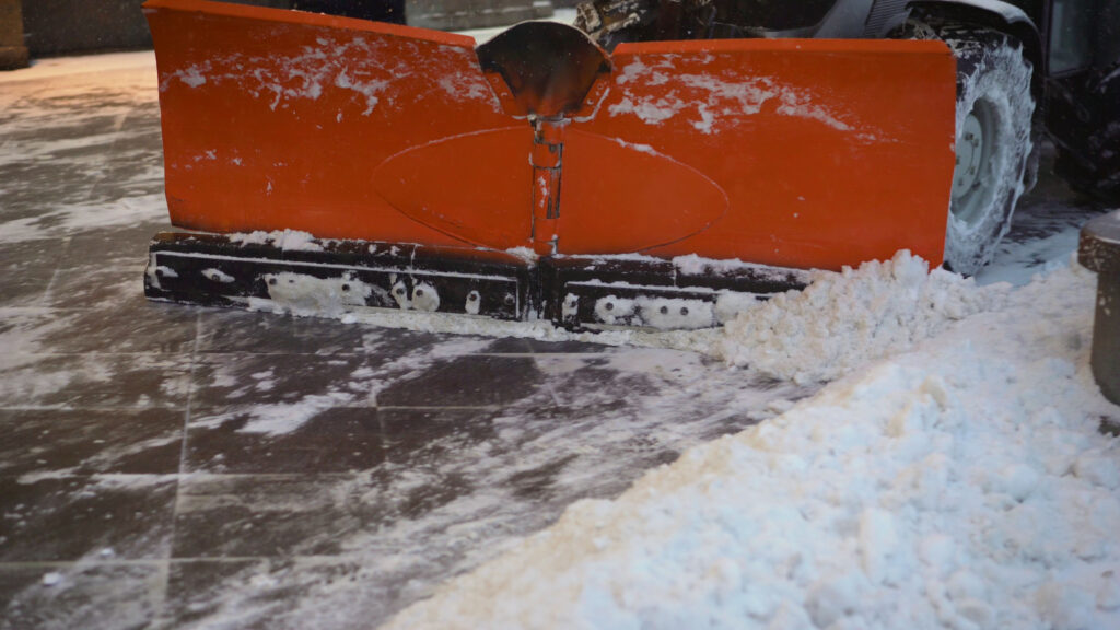 A snowplow with an orange blade clears snow from a paved surface, creating a clean path during winter conditions.