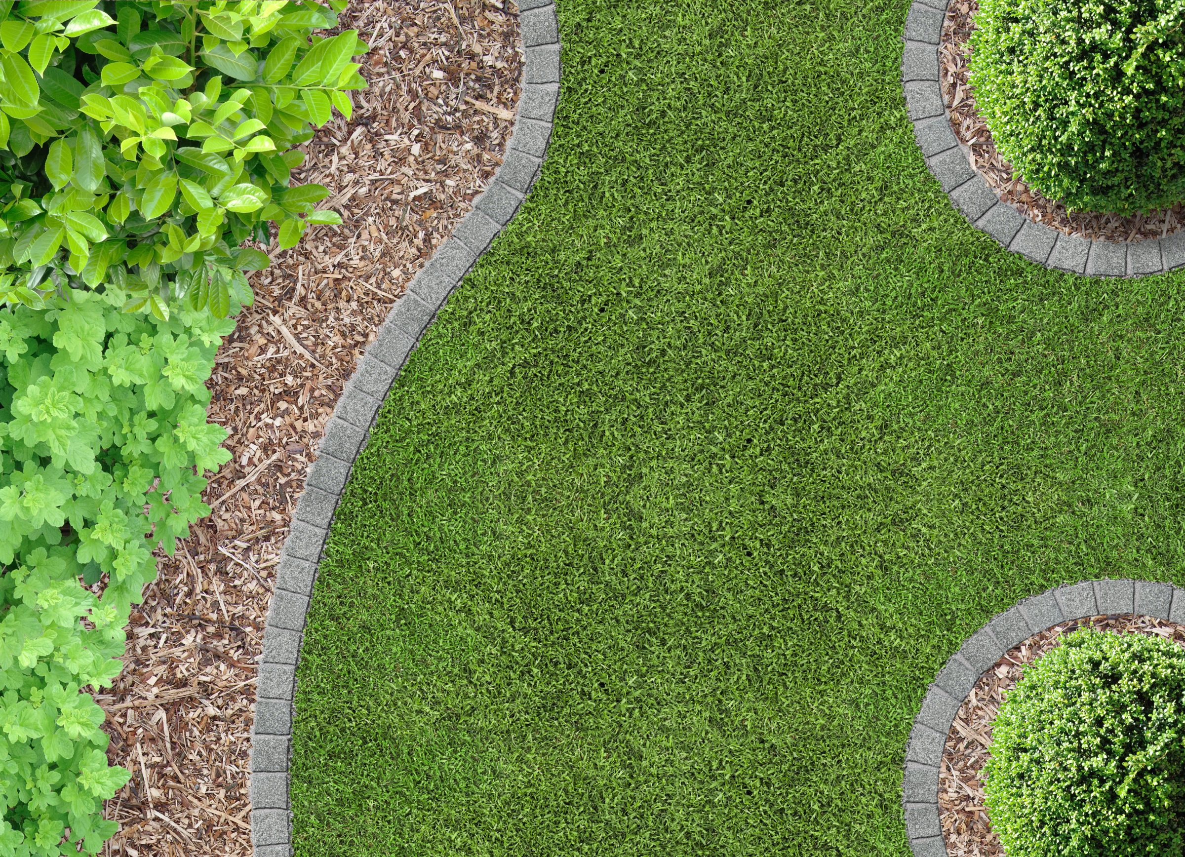 Aerial view of landscaped garden with curved stone pathways, green grass, mulch, and lush shrubs, creating a neat and serene outdoor space.