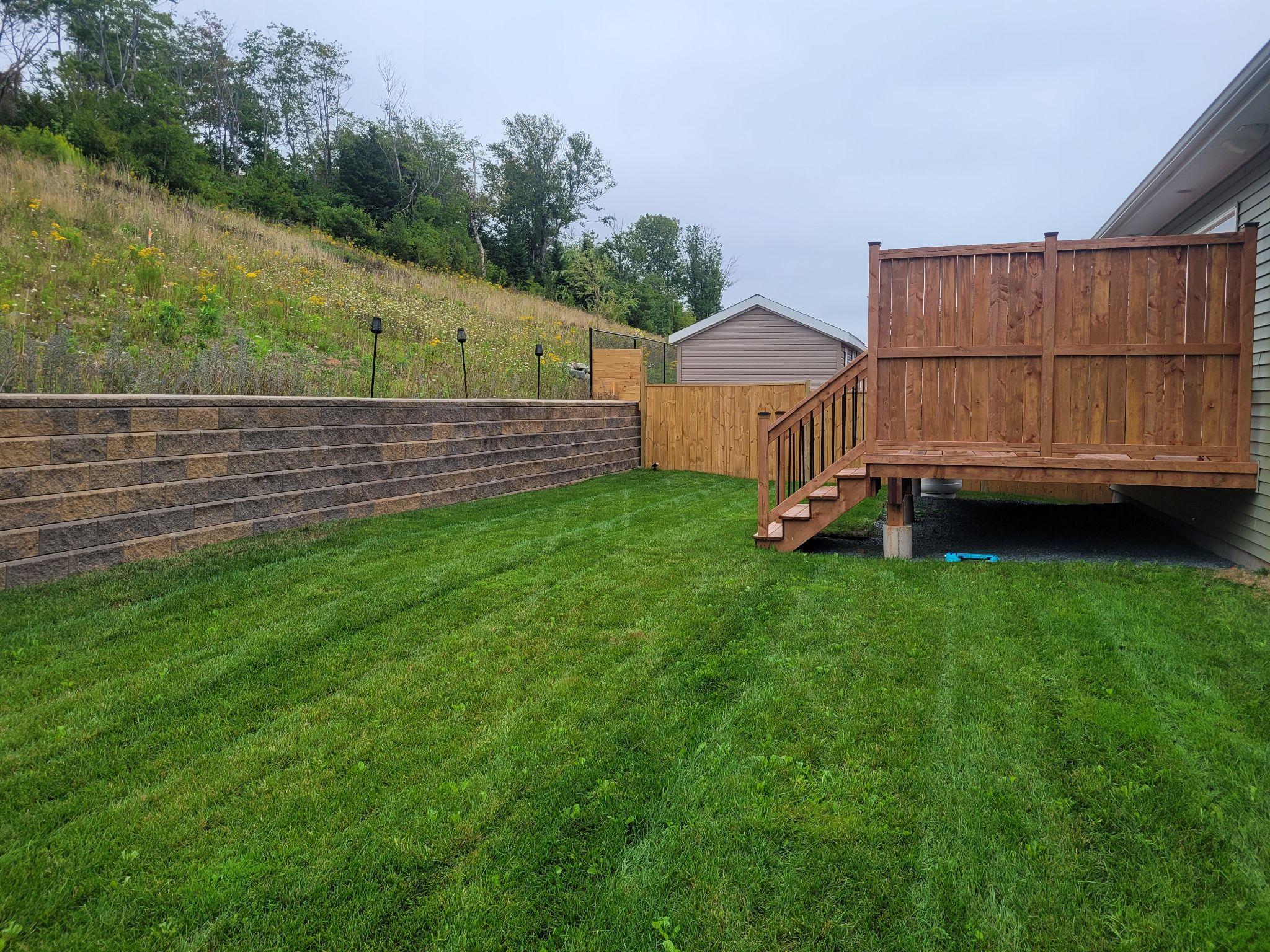 Backyard with retaining wall, wooden deck, and green lawn.