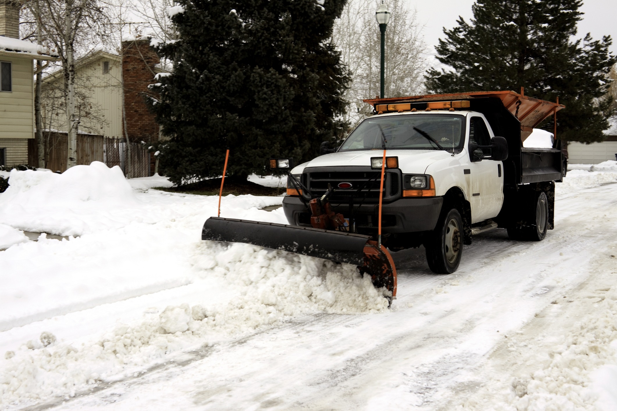 Pickup truck plow clearing packed snow along a residential driveway
