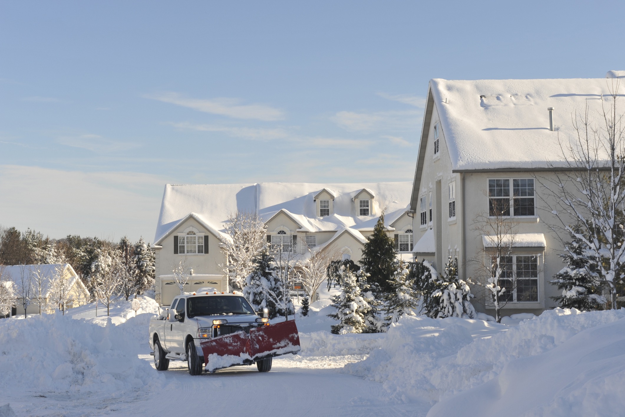 Truck with plow attachment clearing a snow-covered driveway in front of a large house